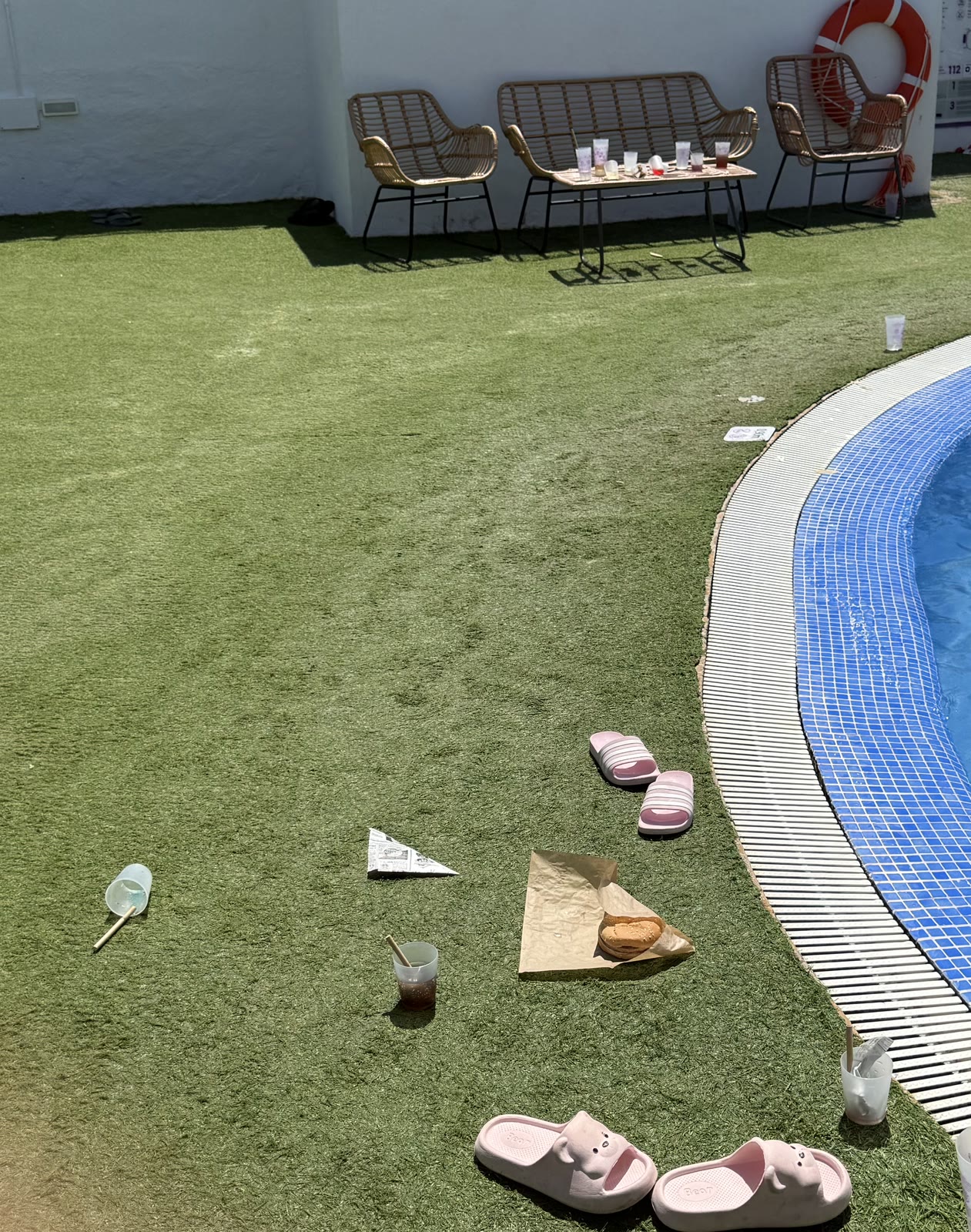 Gots reutilitzables, envasos de menjar i altres objectes fotografiats sobre la gespa artificial al costat de la piscina.