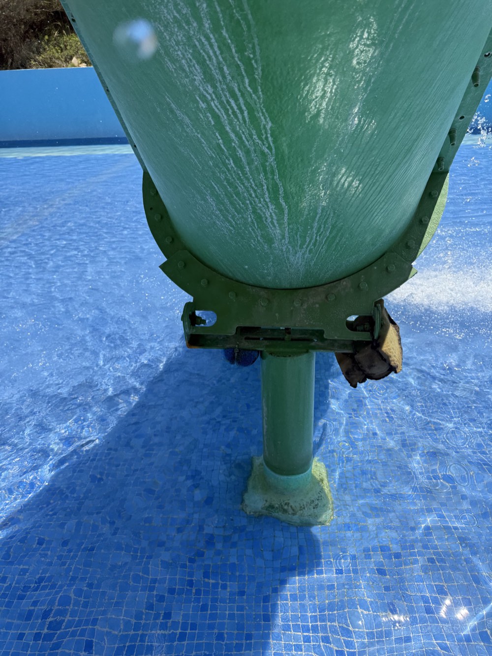 Green-slide support bracket with a protruding metal end and dark material apparently fastened with a plastic cable tie.